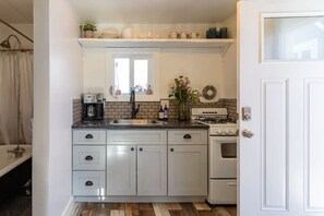 Une cuisine de taille réduite avec des meubles blancs, une cuisinière à gaz, un évier et une fenêtre au-dessus du plan de travail.