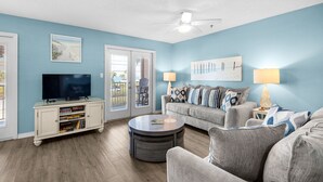 A living room with a TV, sofa, coffee table, and a bookshelf. - Cute 2/2 condo - 2 KING BEDS, Queen Sofa Sleeper and hall bunks (Destin)