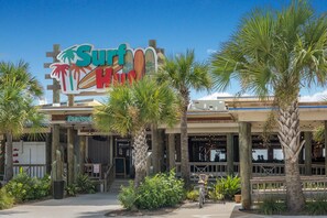 Ein Restaurant namens 'Surf Hut' mit einem Surfbrett-Schild, Außenbereich und Palmen.