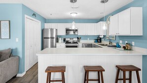 A modern kitchen with white cabinets, stainless steel appliances, and a central island with stools. - Cute 2/2 condo - 2 KING BEDS, Queen Sofa Sleeper and hall bunks (Destin)