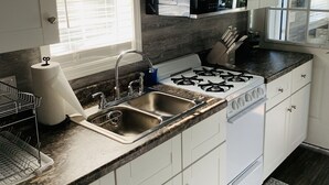 Een moderne keuken met witte kasten, een roestvrijstalen spoelbak, een gasfornuis en een magnetron.