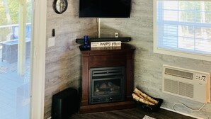 Een woonkamer met een open haard, een televisie aan de muur en een plafondventilator.