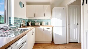 Cocina con armarios blancos, un refrigerador Bosch, lavavajillas, ventana con vistas y un cartel de manta antiincendios.