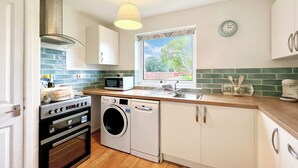 Cocina compacta con lavadora, horno, microondas y ventana con vistas a zonas verdes.