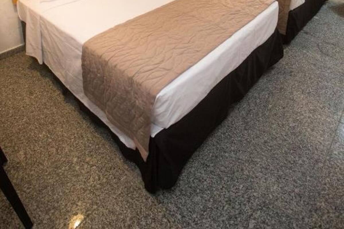 Habitación de hotel con dos camas, cada una con cabecero de madera, ropa de cama blanca y una manta color beige.