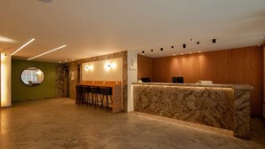 Zona de recepción de hotel con mostrador de mármol, área de estar con sillas y un espejo circular en la pared.