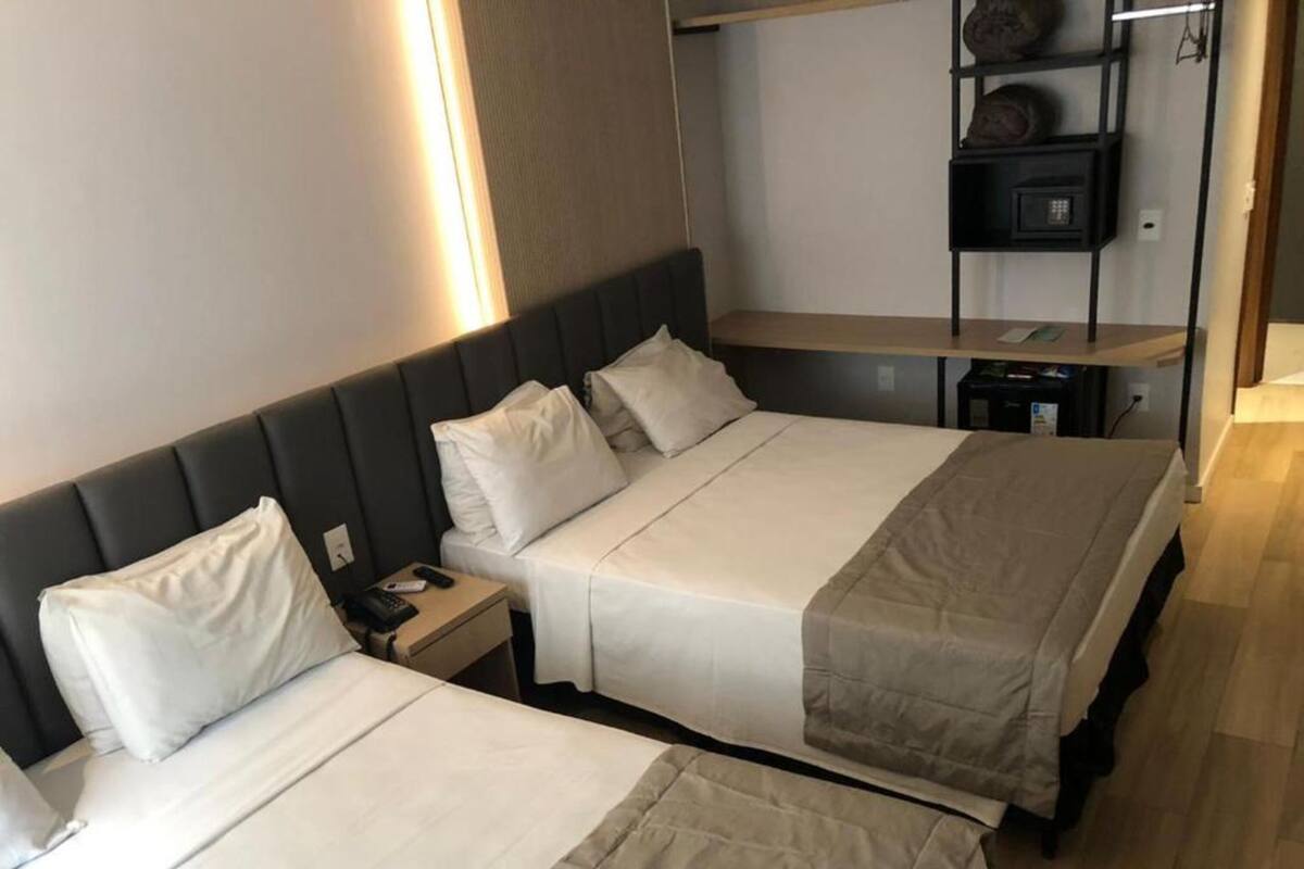 Habitación de hotel con dos camas, una mesita de noche con control remoto y una estantería decorada.
