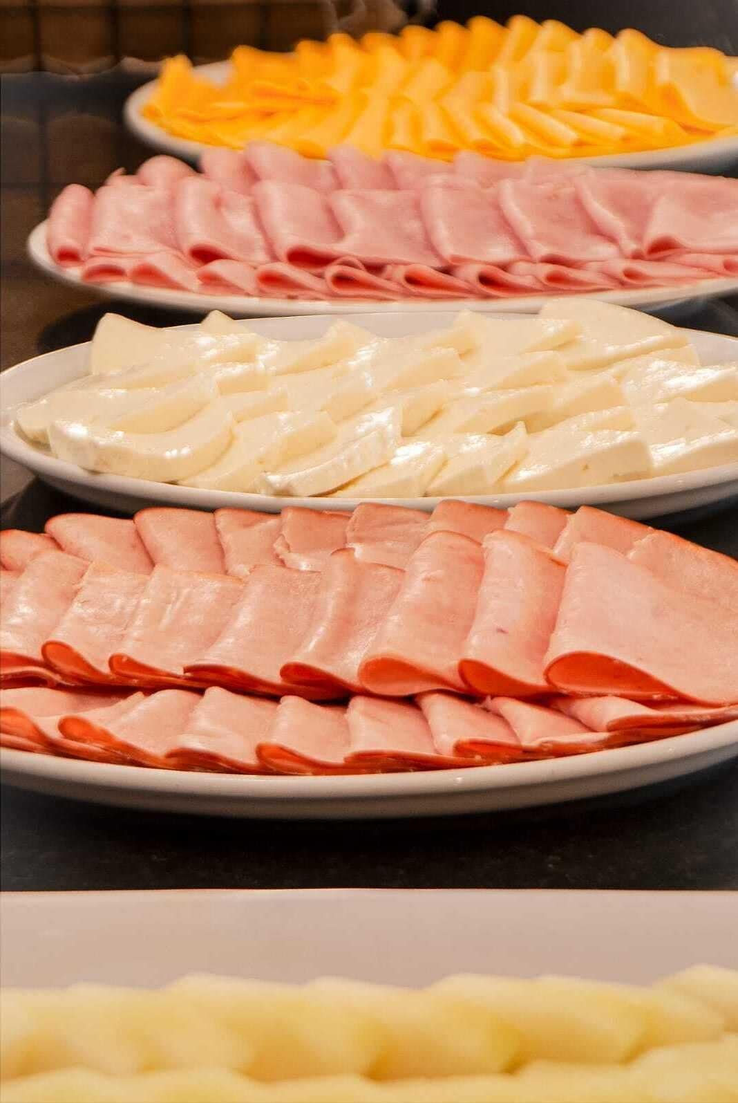 A variety of sliced meats and cheeses arranged on plates.