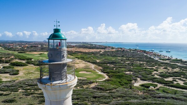A coastal view with a lighthouse, sandy terrain, and a marina with boats.