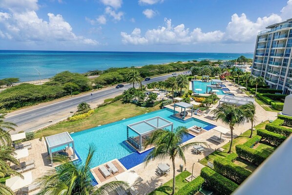 A resort with a large pool, palm trees, and a view of the ocean.