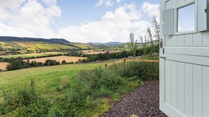 A view from a building with a window, overlooking a rural landscape with fields and distant hills. - Woodside Hut 3 - UK36107 (Strathpeffer)