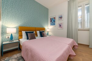 Ein Schlafzimmer mit gemusterten Wänden, einem Bett mit einer rosa Steudecke, zwei Nachttischen mit Lampen und Kunstwerken an der Wand.