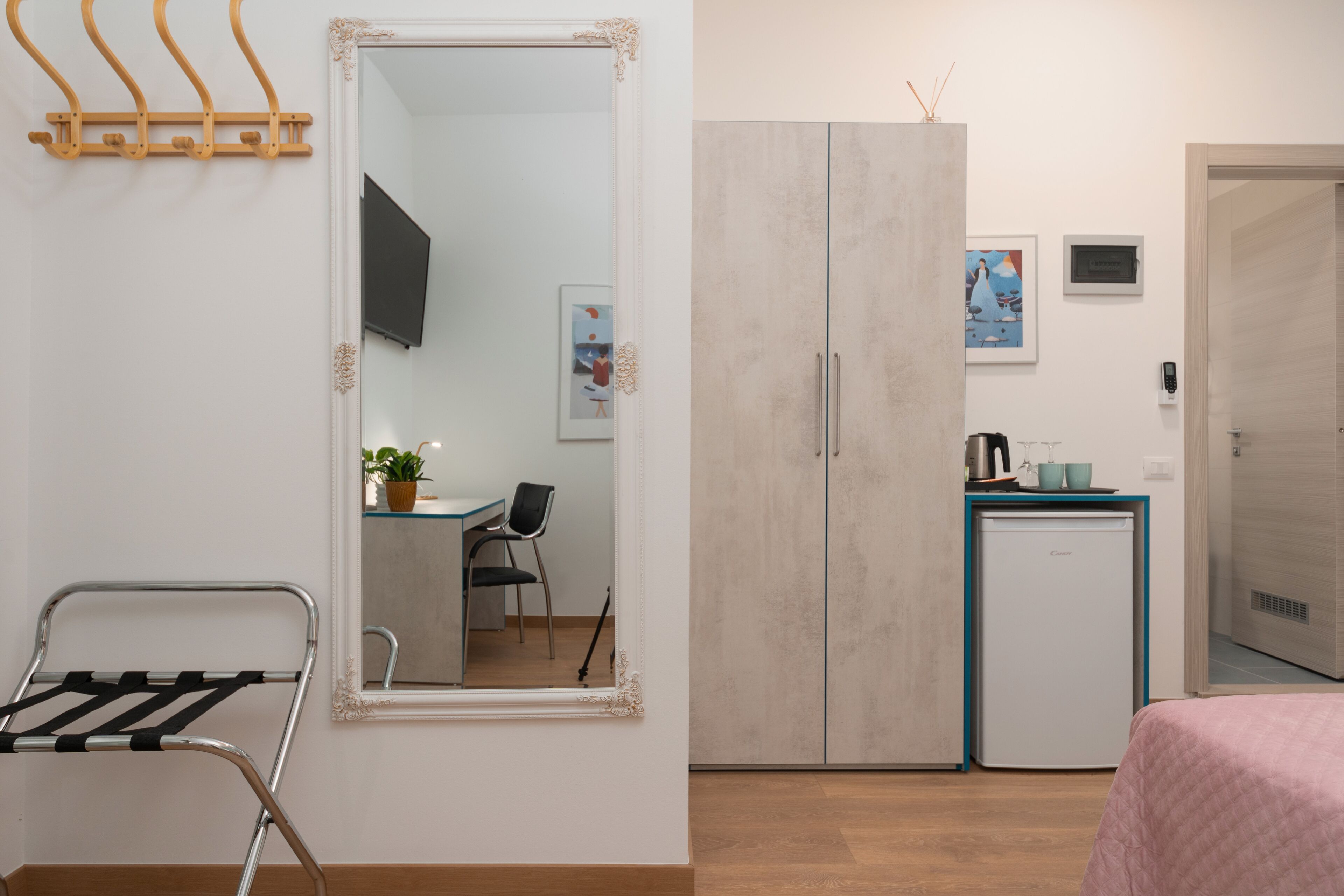 Una habitación compacta con cama, kitchenette pequeño, armario, espejo y zona de estar con una silla y mesa.