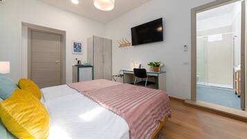 A bedroom with a bed, a desk, a TV, and a sliding glass door to a balcony.