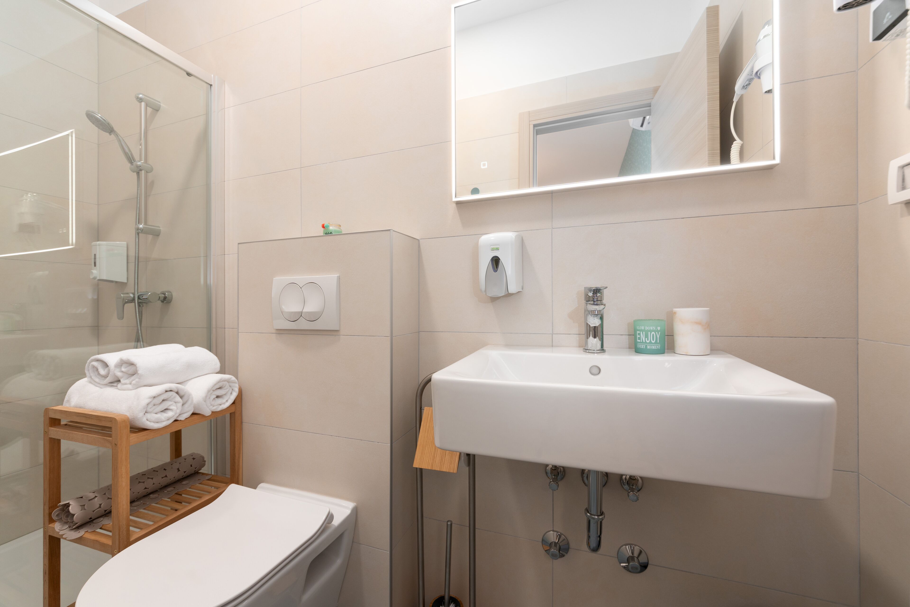A modern bathroom with a glass shower enclosure, a wooden towel rack, a white sink, and a mirror above the sink.
