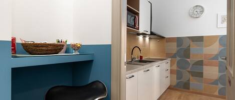 A kitchen with a blue countertop, a black chair, a microwave, and a clock on the wall.