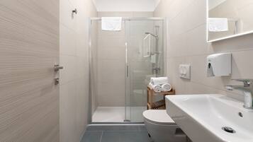 Un baño moderno con cabina de ducha de vidrio, un lavabo blanco y un inodoro.