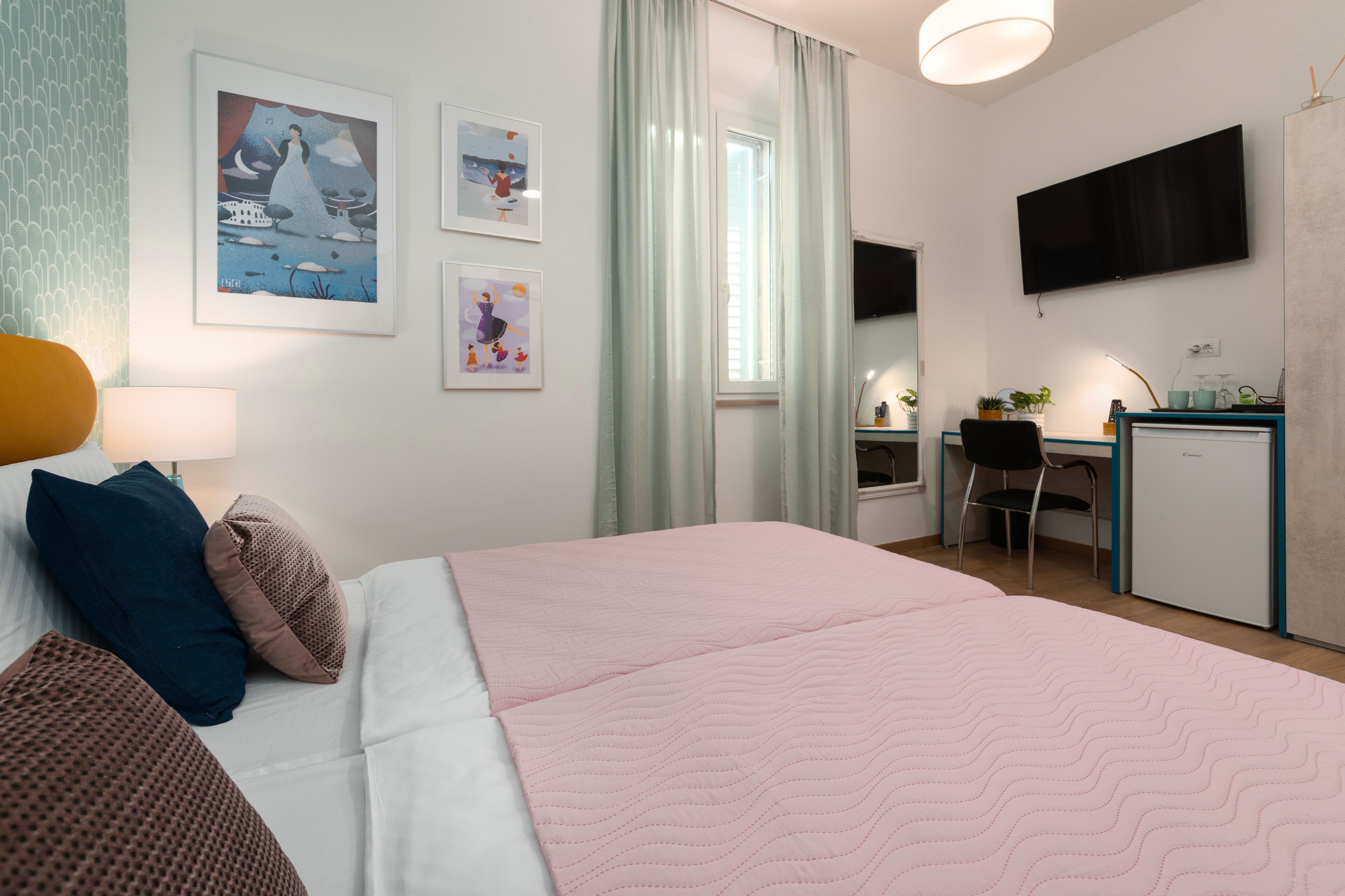 Une chambre d’hôtel équipée d’un lit, d’un bureau, d’une chaise, d’une télévision et décorée avec des œuvres d’art au mur.