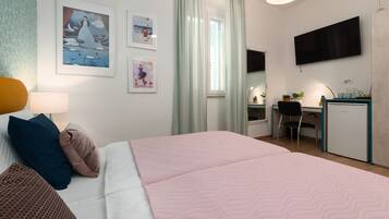 Une chambre d’hôtel équipée d’un lit, d’un bureau, d’une chaise, d’une télévision et décorée avec des œuvres d’art au mur.
