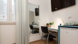 A compact room with a desk, chair, and a small refrigerator. A flat-screen TV is mounted on the wall above the desk. - Polesana Rooms (Pula)