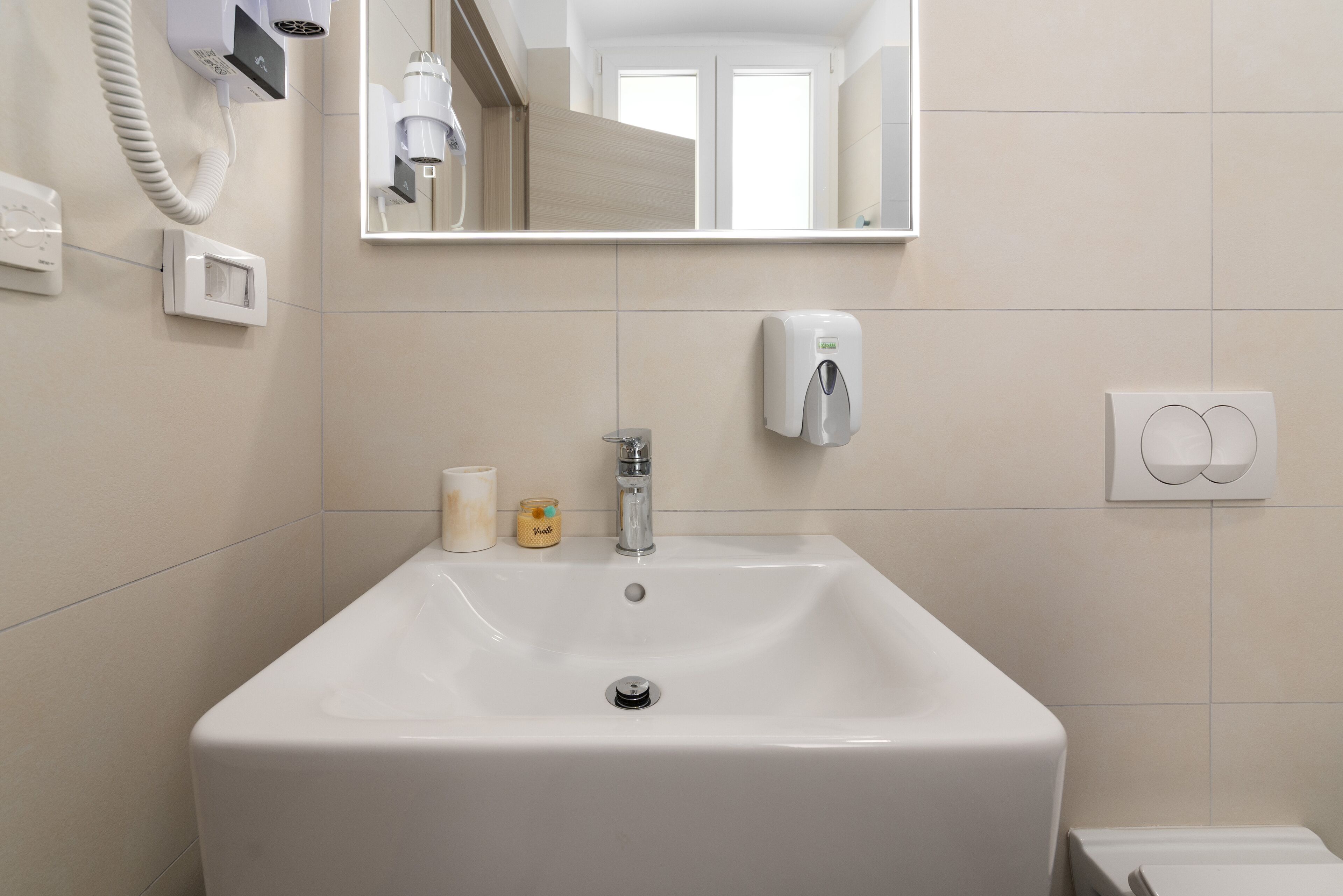 A bathroom with a white sink, a mirror, a hand dryer, and a soap dispenser.