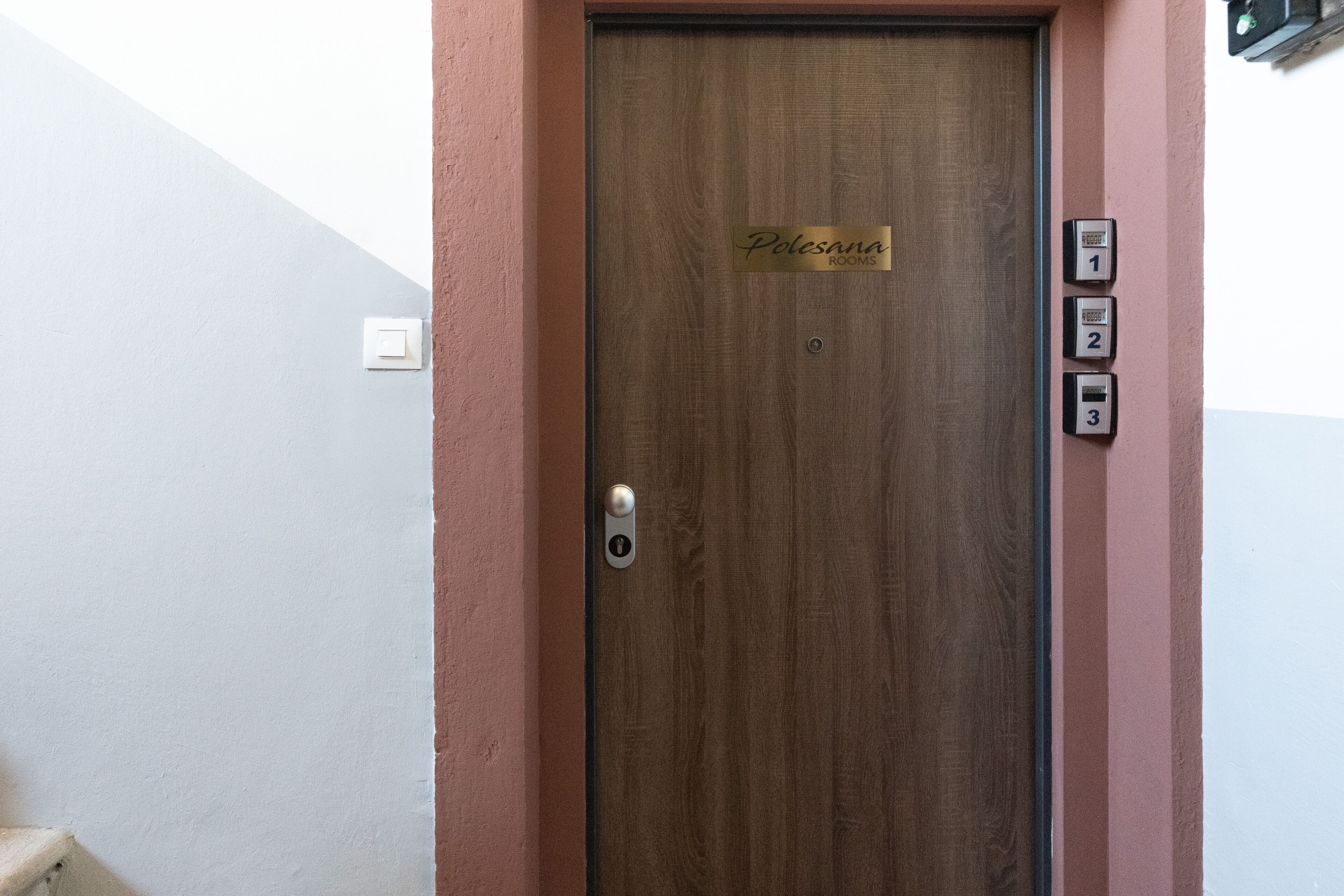 Une porte en bois avec une enseigne indiquant « Polesana Rooms » et trois boutons numérotés sur le côté droit.