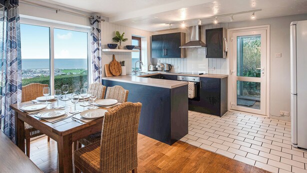 A modern kitchen with a large island, dark cabinetry, and a view of the sea. - Frondeg translates to ’Pretty Hill’, this is exactly what this property offers. (Aberaeron)