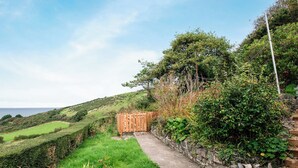 A pathway leading to a wooden gate, surrounded by lush greenery and a stone wall. - Frondeg translates to ’Pretty Hill’, this is exactly what this property offers. (Aberaeron)