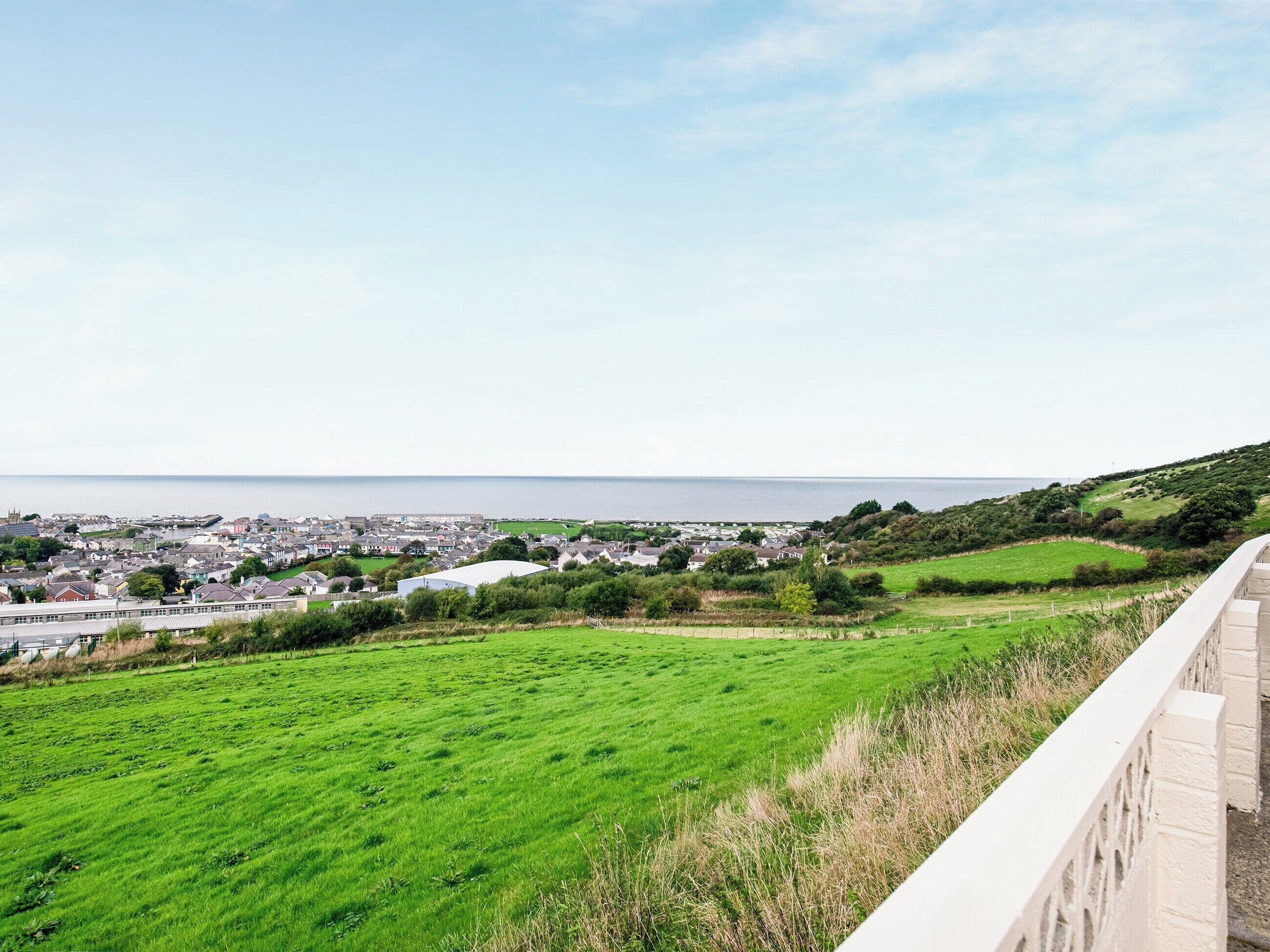 A coastal town with a view of the sea, green fields, and residential buildings.