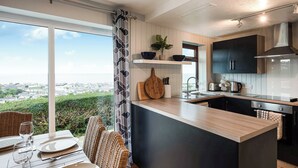 A modern kitchen with a large island, a dining area with wicker chairs, and a view of the city. - Frondeg translates to ’Pretty Hill’, this is exactly what this property offers. (Aberaeron)