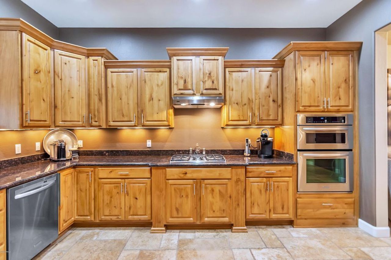 A kitchen with wooden cabinets, a stainless steel refrigerator, a built-in oven, and a granite countertop.