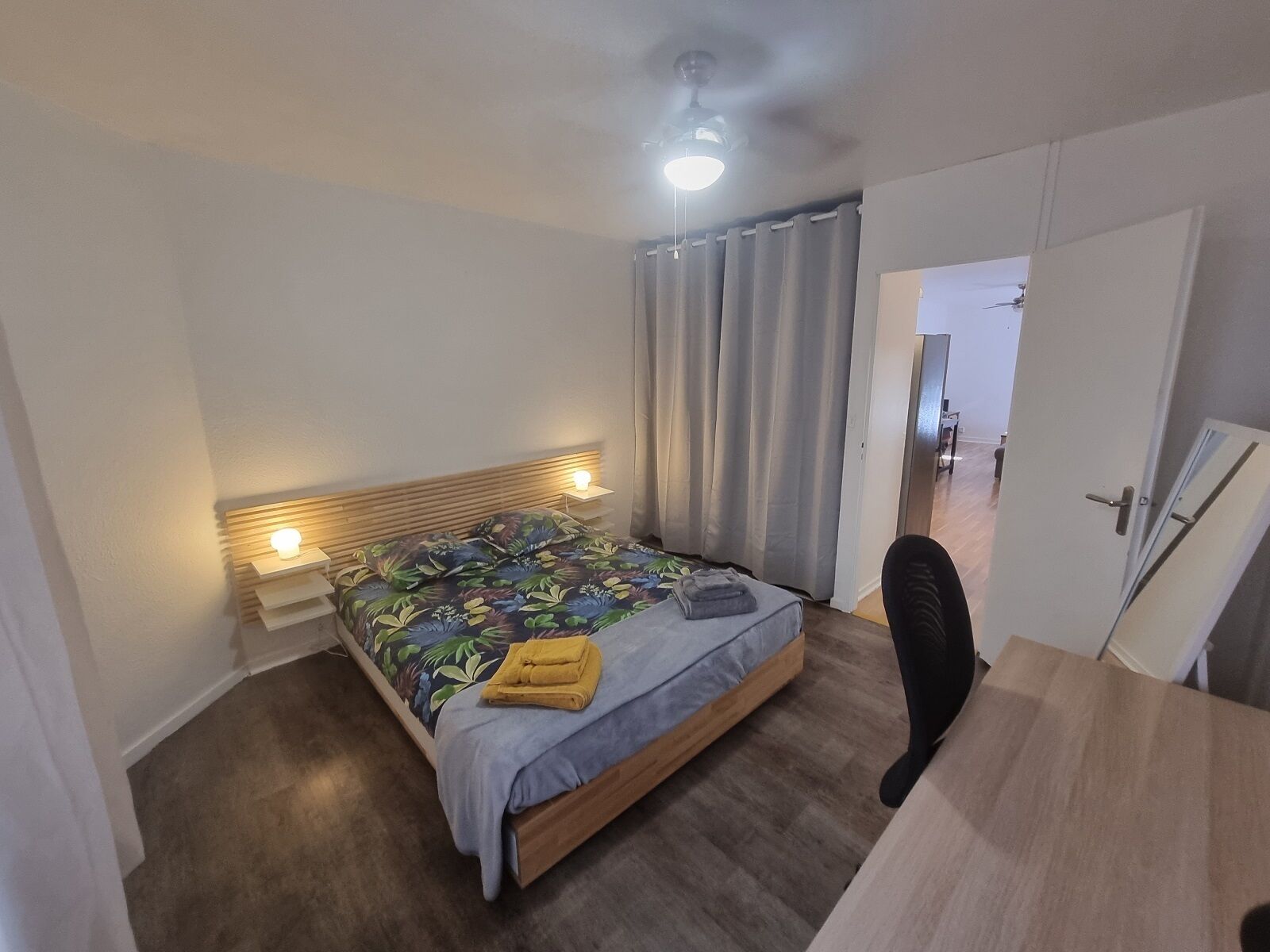 Een slaapkamer met een bed, bedlampen, een plafondventilator en een deur naar een andere kamer.