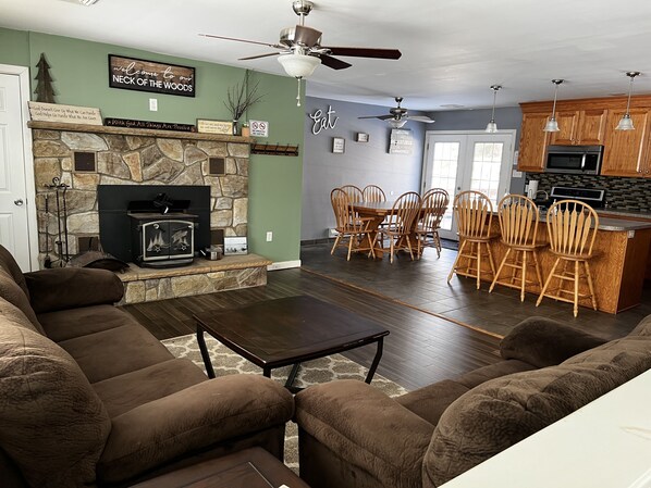 A living room with a fireplace, a dining area with wooden chairs, and a kitchen with wooden cabinets and a microwave.