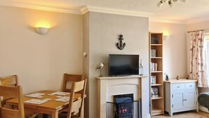 A cozy living room with a fireplace, a dining table with chairs, a bookshelf, and a television on a mantel. - 2 bedroom accommodation in Morecambe (Morecambe)