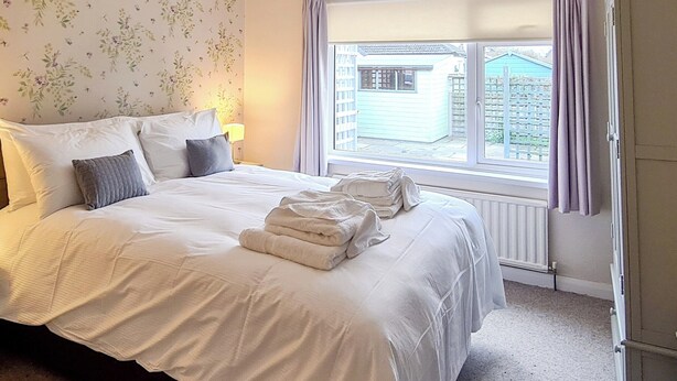 A neatly made bed with white linens and pillows, a window with curtains, and a radiator. - 2 bedroom accommodation in Morecambe (Morecambe)