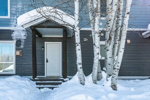 Una casa de exterior oscuro, una puerta blanca y un patio delantero cubierto de nieve.