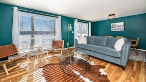 Una sala de estar con paredes color turquesa, un sofá azul, una mesa de centro de vidrio y un tapete de cuero de vaca.