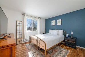 A bedroom with a bed, bedside table, nightstand, and a window with curtains.
