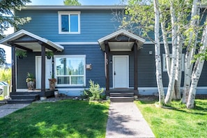 A two-story house with a front porch, a garage, and a small front yard with a tree.