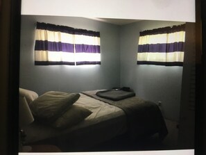 Ein Schlafzimmer mit einem Bett, einem Nachttisch und zwei Fenstern mit gestreiften Vorhängen.