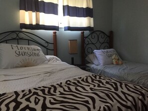 Zwei Einzelbetten mit Zebra-Muster-Decken, ein Nachttisch mit Lampe und Vorhänge mit Streifenmuster.