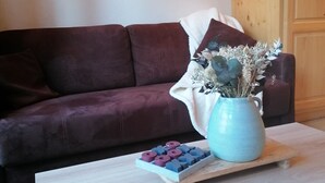 A living room with a dark brown sofa, a light wooden coffee table, and a decorative vase with dried plants. There are two wall-mounted lamps and a geometric wall art piece. - Duplex Apartment "The 529  (Bourg-Saint-Maurice)