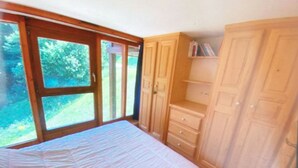 A bedroom with a bed, wooden wardrobe, and a window with a view of greenery. - Duplex Apartment "The 529  (Bourg-Saint-Maurice)