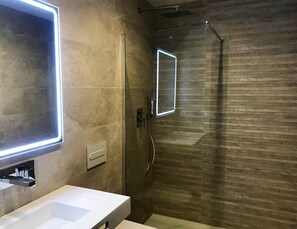 Bathroom features a large mirror, glass-enclosed shower, and wall-mounted faucet.