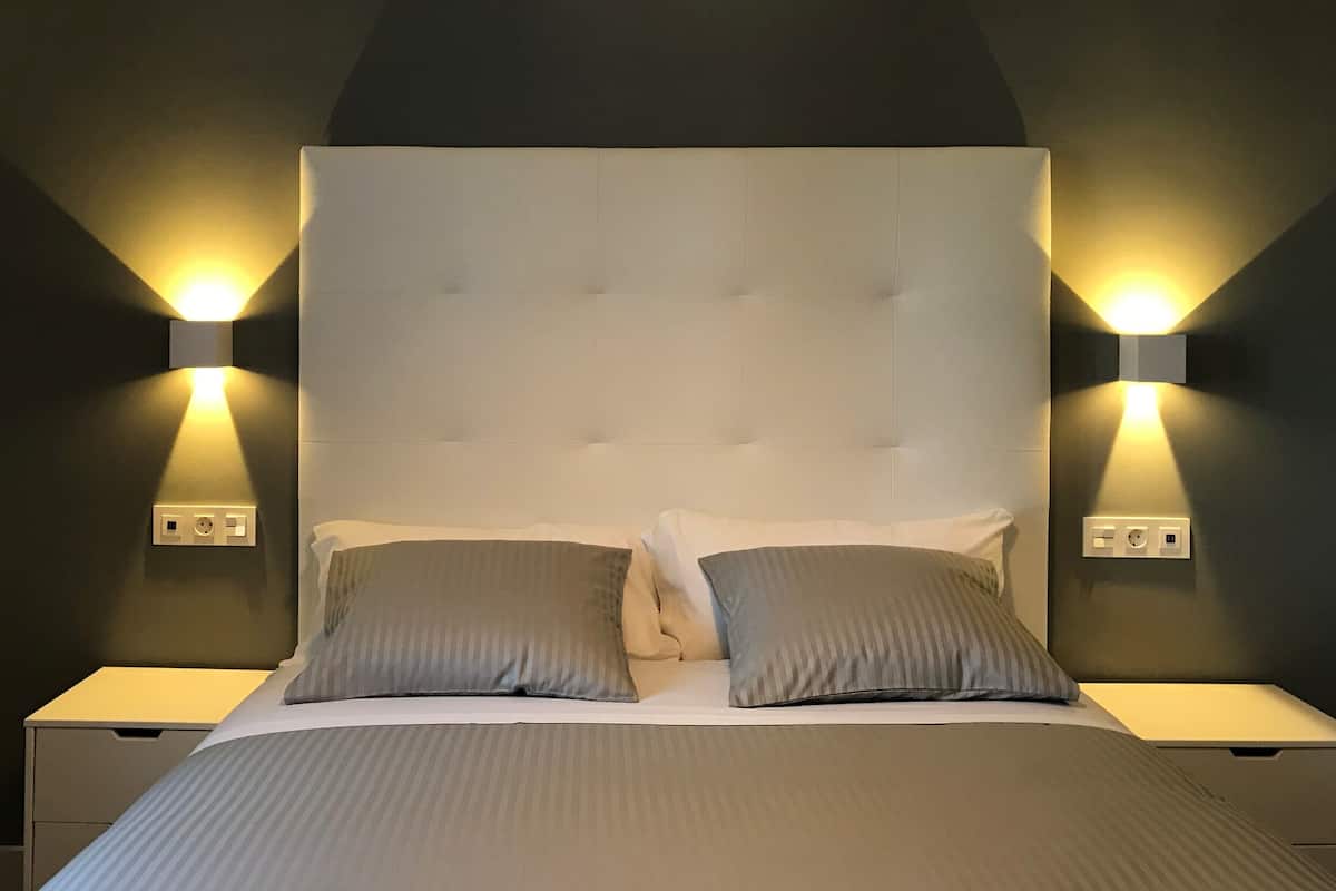 A bedroom with a tufted headboard, two bedside lamps, and a bed with grey bedding.