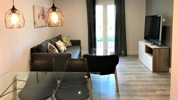 A modern living room with a sofa, two pendant lights, a flat-screen TV, and a glass dining table. - Apartamentos Ciudad de Ronda (Ronda)