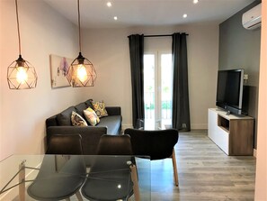 A modern living room with a sofa, two pendant lights, a flat-screen TV, and a glass dining table. - Apartamentos Ciudad de Ronda (Ronda)