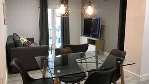 A modern living room with a glass dining table, black chairs, a grey sofa, and a flat-screen TV. - Apartamentos Ciudad de Ronda (Ronda)