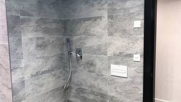 En modern dusch med ett handhållet duschmunstycke och en väggmonterad kontrollpanel.