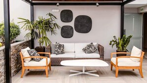 A modern outdoor seating area with a white sofa, two wooden chairs, and a white table. There are three large abstract wall art pieces above the sofa. - Exclusive Apartments in Pedro Martinto by Wynwood-House (Lima)